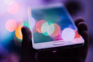 Hand holding a smartphone. Colorful lights reflected on the surface.